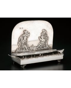Sofa-style with hinged lid revealing row of eight receptacles with spouts. Back plate featuring imagery of Pan and Cupid; leaves projecting on two sides. Set on four scroll-supports. Marked. 4 x 4.5 inches.