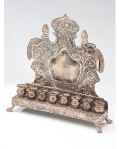 Cartouche form backplate with convex center featuring Menorah flanked by crouching lions; fronted by bench supporting eight oil/candle holders; the whole set on four animal paw supports. Marked: “Fraget.” 9 x 9 inches.