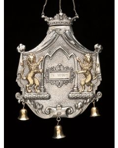 Cartouche-form with cut scalloped borders above crown, rampant lions flanking a hinged compartment that holds a plaque inscribed in Hebrew. Hung with three bells, suspension chain above. 6 x 5 inches.