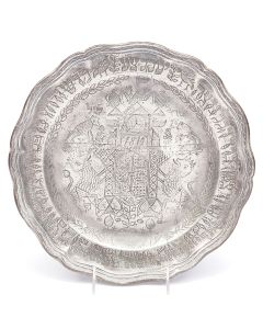 Round plate with scalloped raised rim bearing the order titles of the Passover Seder, engraved in Hebrew. In center, elaborate clock tower design - bearing date - flanked by stylized rampant lions, flora and fauna. Diameter: 12.25 inches.