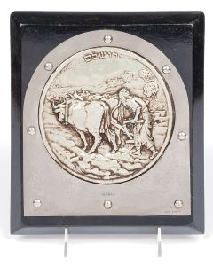 Of arched design riveted to wooden base, embossed with high relief depiction of a farmer working his land, with Hebrew title below. Marked: “Bezalel Jerusalem.” 9 x 8 inches.