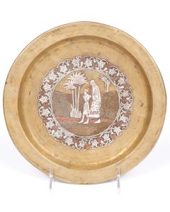 Round plate with raised rim featuring central image of Biblical figures Abraham and Isaac; with arabesque scrolling and grape and leaf tendrils. Metal label on reverse: “Bezalel Jerusalem.” Diameter: 9 inches.