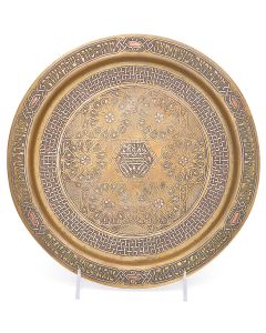 Round plate with raised rim featuring Biblical verses relating to Passover. Geometric decoration with arabesque scrolling tendrils; in center: “Bezalel” below stylized, seven-branch menorah. Diameter: 11.75 inches.